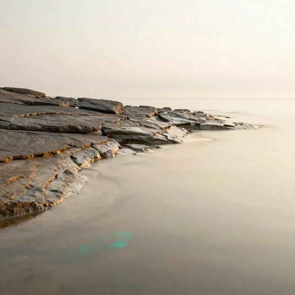 Rock shelf and misty tide pools at dawn with calm open water below.
